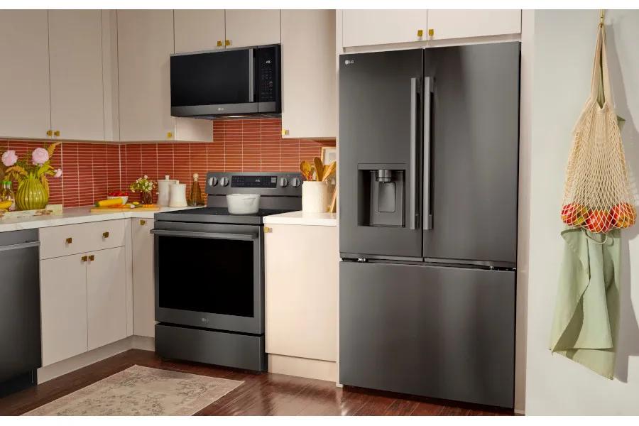 LG black stainless steel French door refrigerator with ice and water dispenser alongside an LG black stainless electric range with over-the-range microwave, set in a bright kitchen with cream cabinets, red tile backsplash, and fresh produce on the counter.