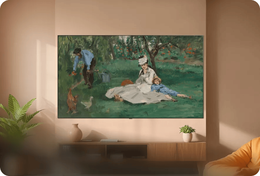 LG TV mounted on a warm-toned wall in a living room, displaying a classic impressionist painting of a family in a garden, with a wood media console, plants, and an orange chair visible in the room