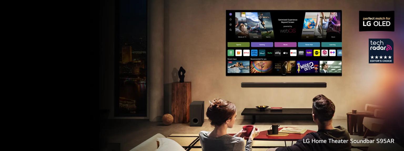 An LG TV  equipped with a matching soundbar displays various content options as a man and woman look on. “Perfect match for LG OLED” and “Tech Radar Editor’s Choice” badges. Text below reads “LG Home Theater Soundbar S95AR”.