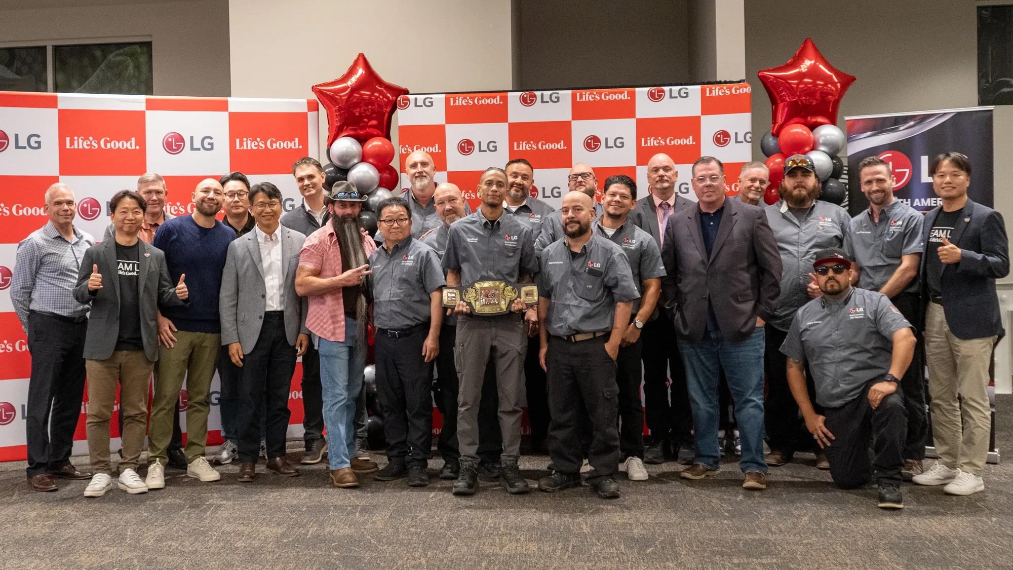 More than two dozen technicians, judges and LG representatives pose in front of LG “Life’s Good” backdrops and red star balloons, with Jonathan Polanco holding the 2026 Champion belt in the center.