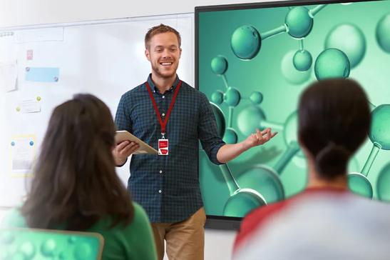 A salesman smiles as he gestures to an LG CreateBoard. A small audience watches his demo, facing away from the camera.