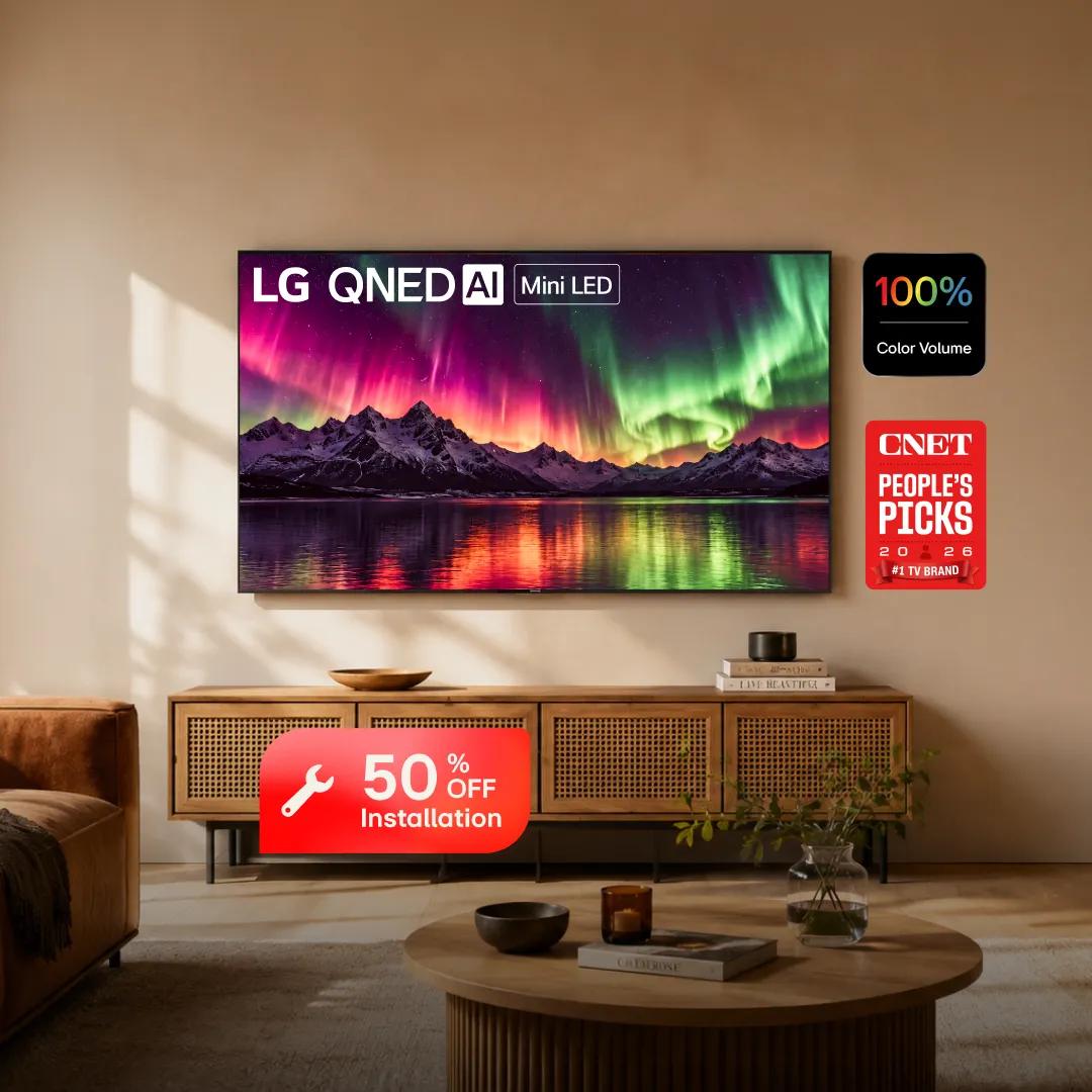 Wall-mounted LG QNED AI Mini LED TV displaying a vivid aurora borealis over snowy mountains and a lake, in a warm, cozy living room with a woven-front media console and round wood coffee table. Badges show "100% Color Volume" and "CNET People's Picks 2026 #1 TV Brand," with a "50% OFF Installation" badge in front of the console.