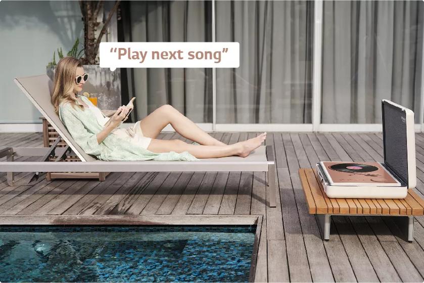 A person lounges by the pool while listening to music on the TV. Text: Play next song.