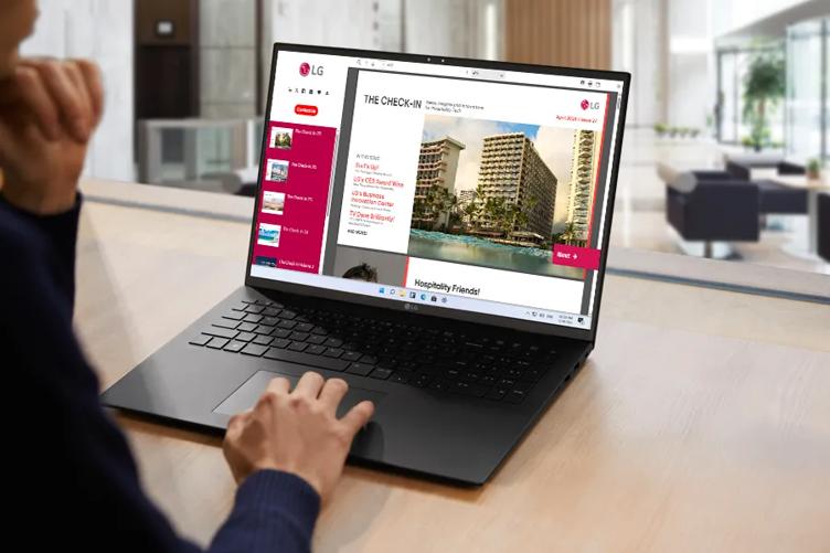 A person reading a laptop on a hotel lobby desk, with LG's Check-In newsletter displayed on the laptop screen
