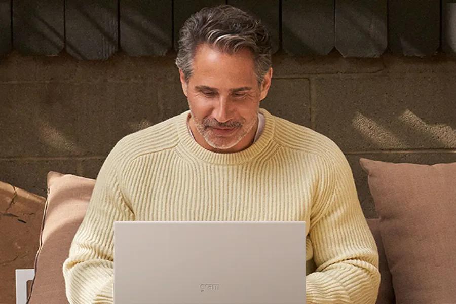 Man in a yellow sweater using a laptop outdoors.