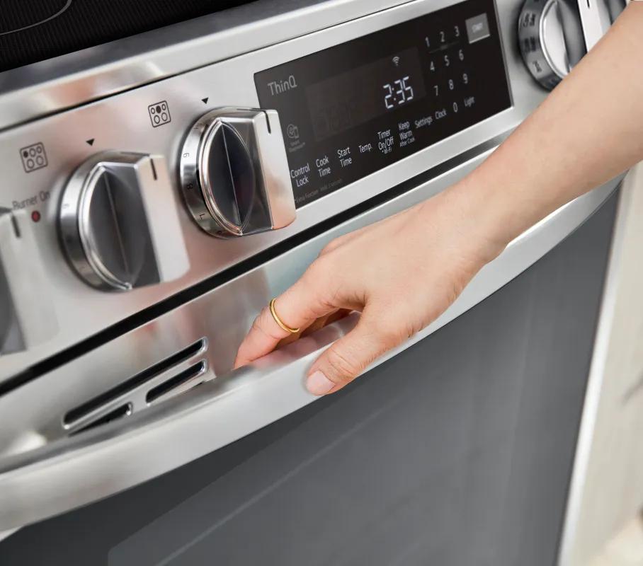 A close-up of the LG range controls and panel with a hand reaching for the oven PrintProof finish handle.