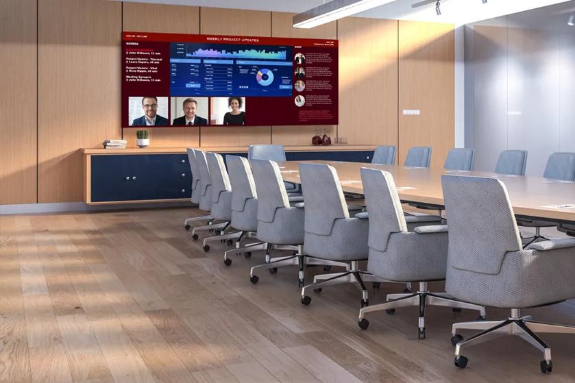 A conference room with DVLED display on the wall displaying a series of business graphs above video conference attendees. 