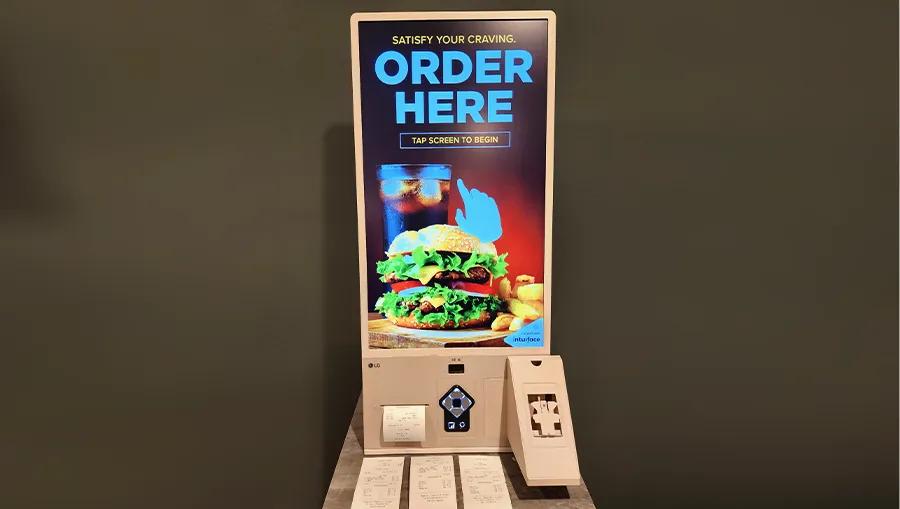 A touch kiosk display in the LG LA Business Innovation Center, advertising a touch screen to order a hamburger meal. 