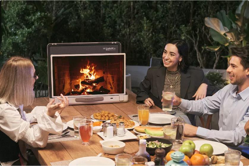 A group of friends enjoys a meal with the TV displaying a fireplace on screen.