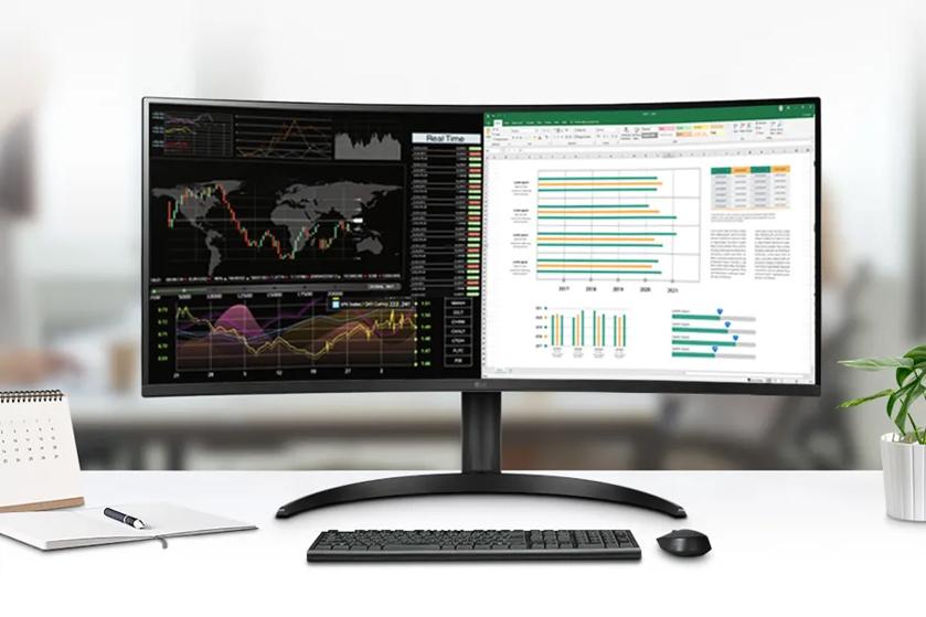Curved monitor displaying financial data and a spreadsheet, on an office desk with a notebook, pen, calendar, and plant.