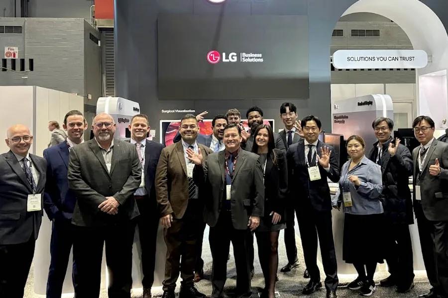 A group of LG businesspeople in business attire standing together at a tradeshow, with an LG Business Solutions sign in the background.