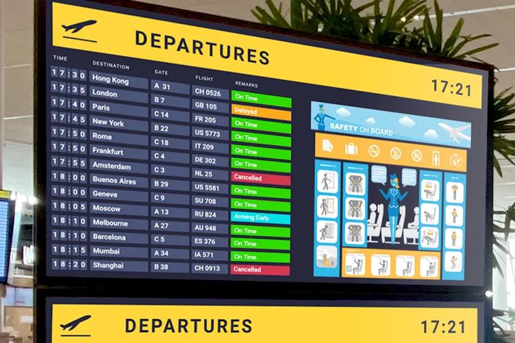 A large signage display in an airport terminal shows the latest arrival and departure times and alerts passengers to safety protocols.