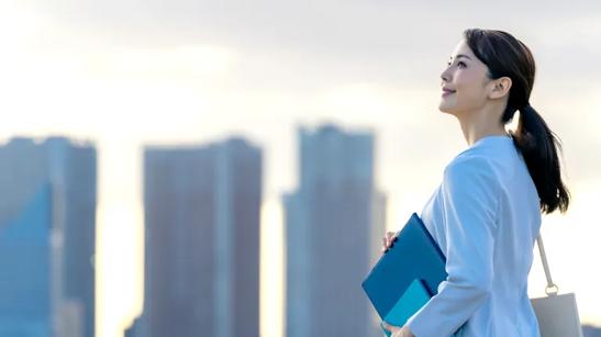 A woman in business casual holding a clipboard and notebook, smiling as she looks at the Chicago city bulidings around her.
