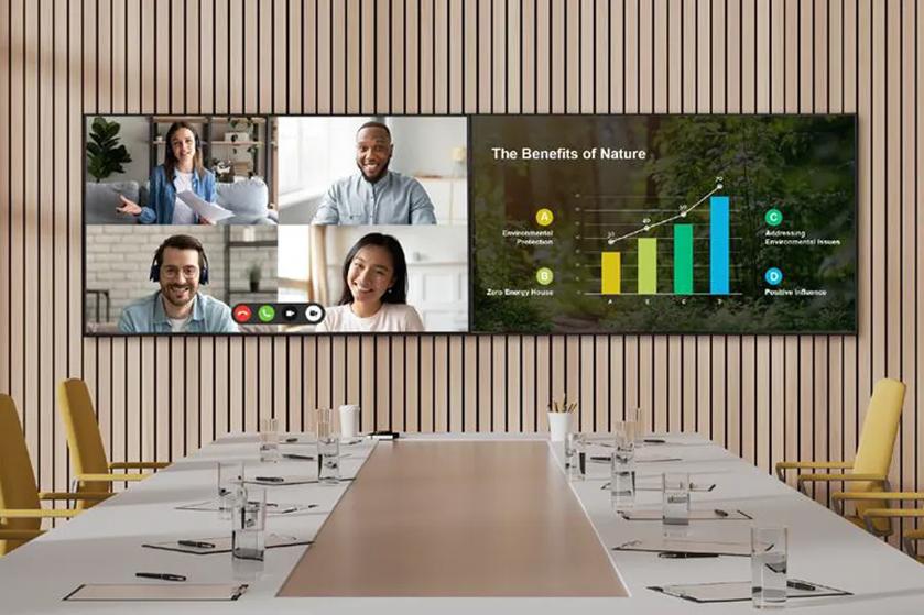 A conference room with video call and bar graph on two wall-mounted screens.