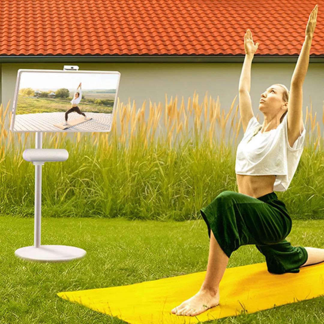 A woman does a yoga lunge outdoors while following a class on StanbyME 2 with XTS speaker.