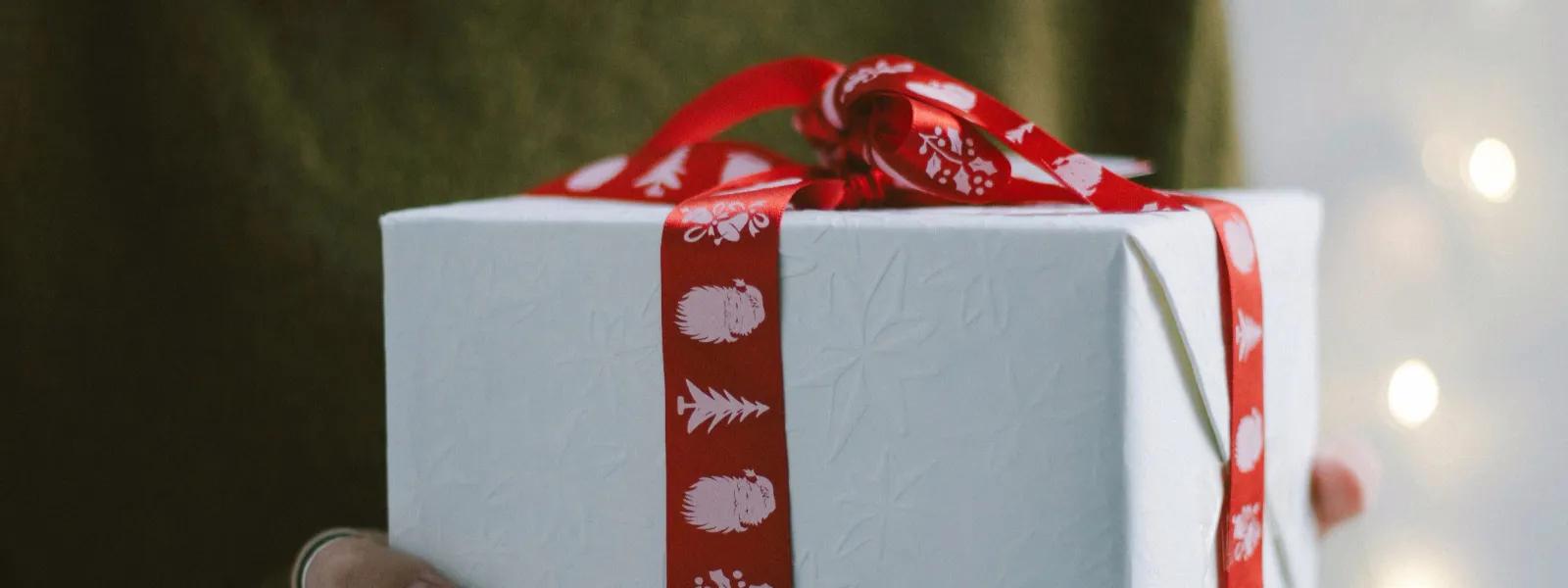 Hands offering a gift box with a decorative red ribbon, embodying the thoughtfulness behind luxury tech gifts and gadgets for her.
