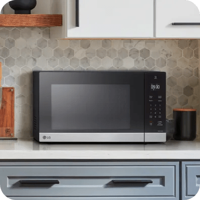 LG countertop microwave on a kitchen counter, shown front-on with a dark window, stainless trim and right-side touch controls above drawers.
