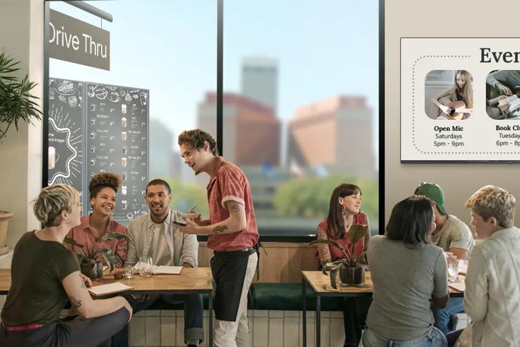 A waiter takes orders in a café full of happy customers. LG displays on the walls and outside the window show menu options and upcoming events. 