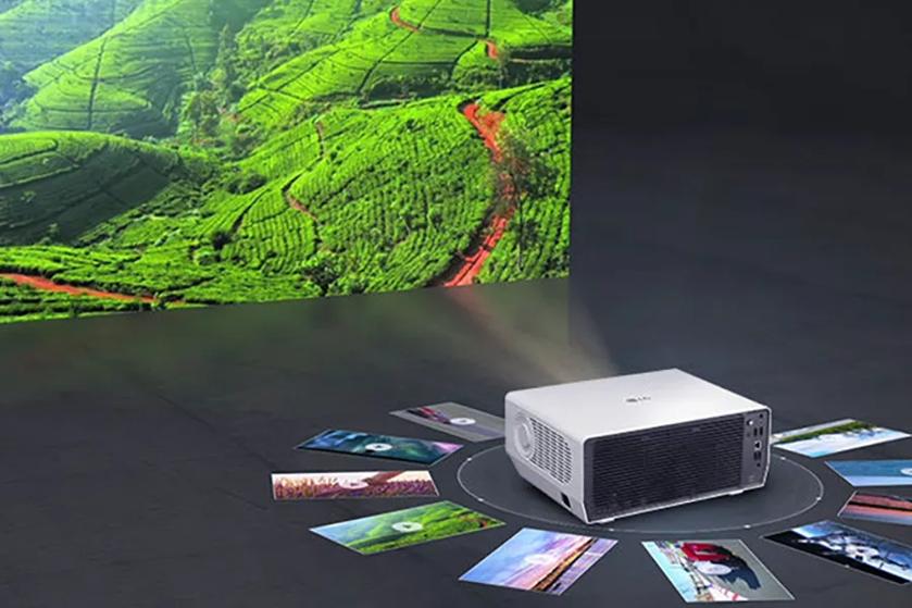 A white projector displaying an image of green terraced fields, surrounded by arranged photographs on a dark surface.