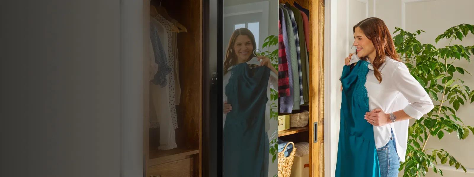 A woman holds a dress on a hanger in front of the LG Styler®’s mirrored door finish.