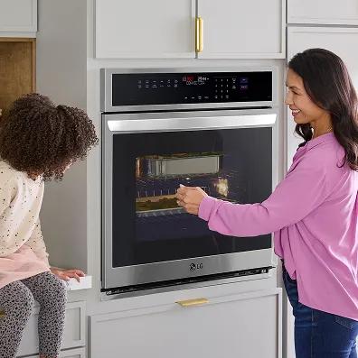 A woman and young girl smile while watching food cook inside an LG wall oven.