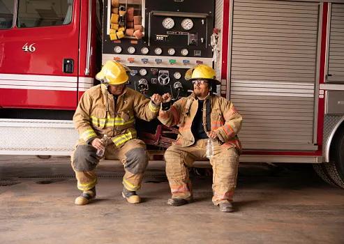 Two male firefighters drink some water after a long day at work.