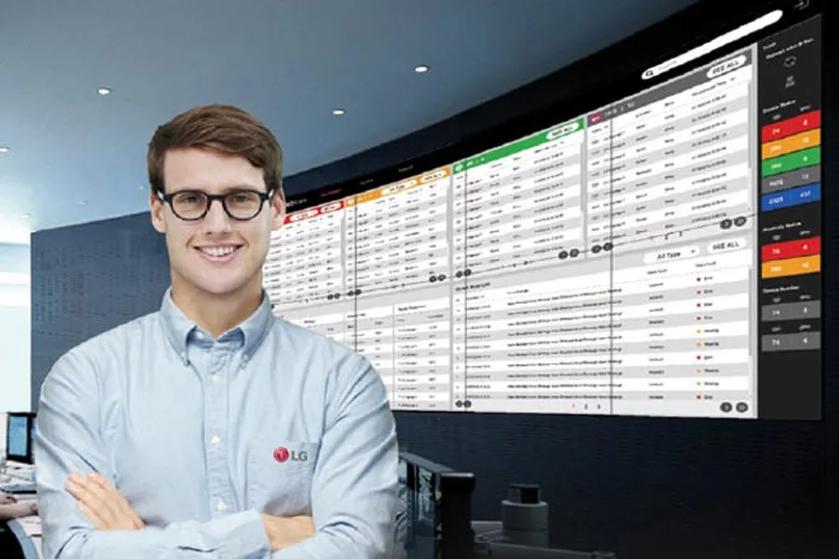 The image depicts a man with glasses and short brown hair standing in front of a large, curved digital display. He is wearing a light blue button-up shirt with the LG logo on the chest. The background features a wide digital screen filled with multiple columns of data, resembling a control room or data center interface. The screen has several colored tabs at the top, each associated with different sections of the data. There are also vertical color-coded bars to the right, possibly indicating various categories or priority levels. The overall setting is high-tech and modern.