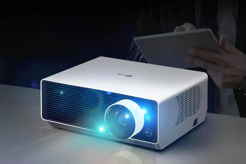 A white LG projector with a bright lens on a reflective surface.