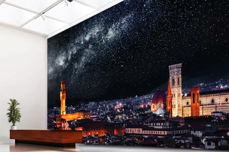 A modern lobby with an ornamental plant and a wooden desk. The large wall behind the desk is covered entirely by an LG Direct View LED Ultimate Business Display, showing a starry night in a scenic city. 