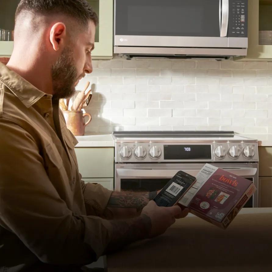 A man sitting in the kitchen using the ThinQ app on is phone to scan the bar code of a frozen meal.