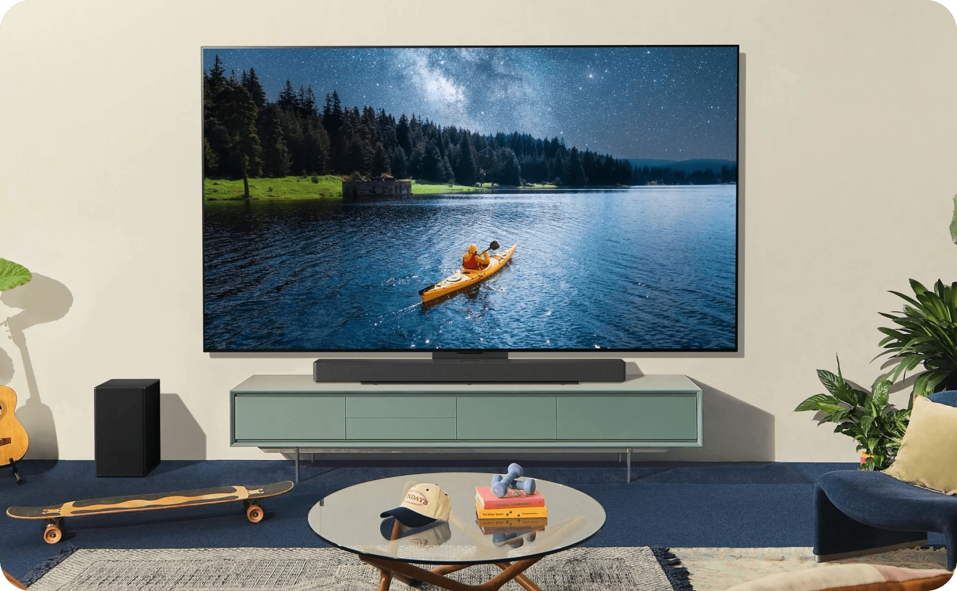 Casual living room with skateboard and guitar, TV shows kayak lake scene with LG soundbar and subwoofer.
