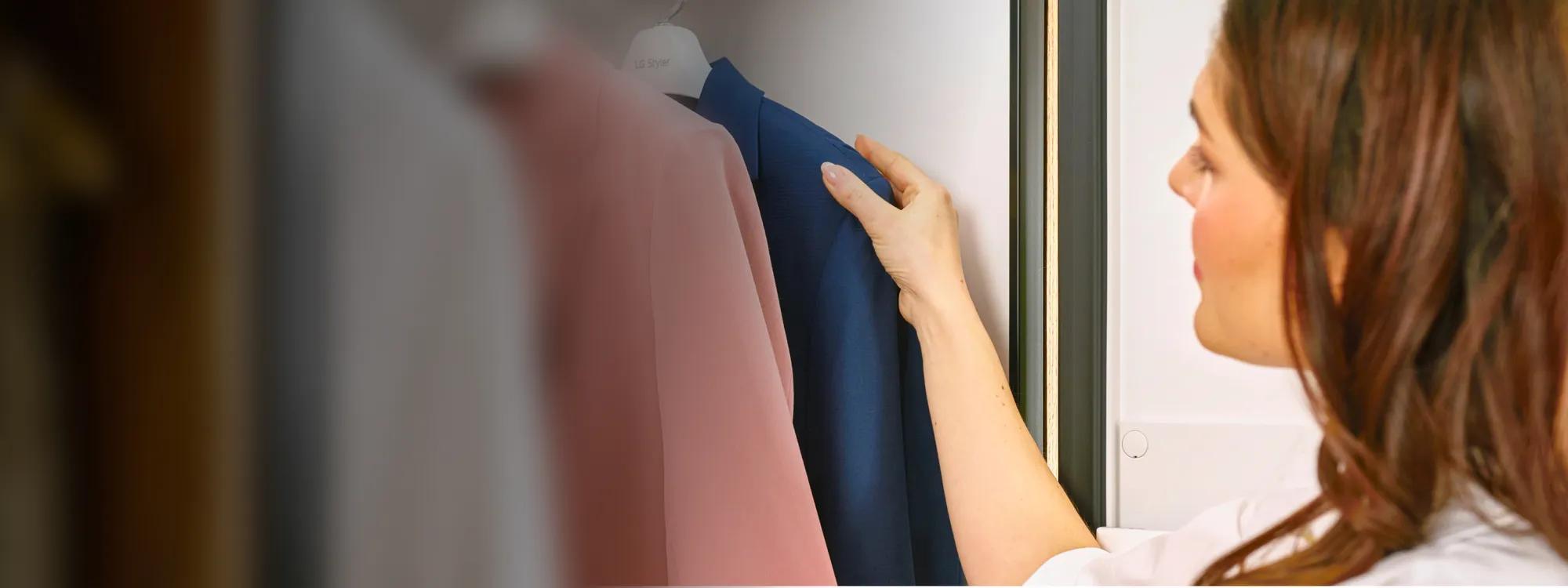 A woman holds a dress on a hanger in front of the LG Styler®’s mirrored door finish.