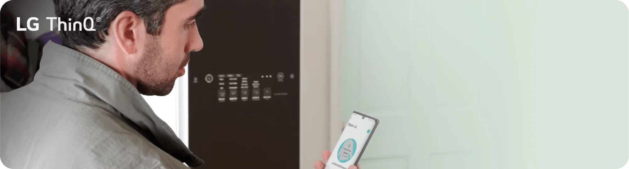 A man stands in front of his LG Styler® and views key settings via the ThinQ® app on his smartphone.