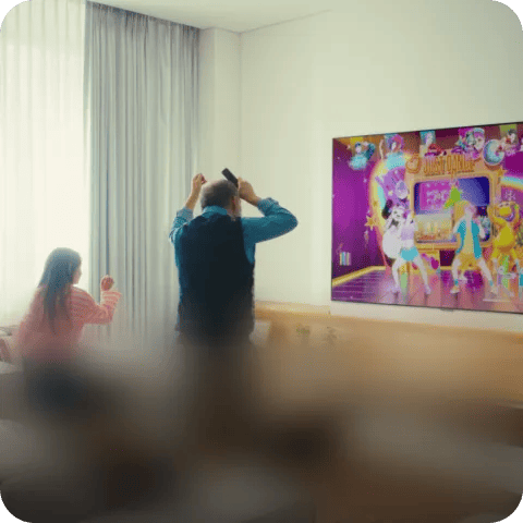 Two people playing a motion-controlled dance game on an LG TV in a living room.