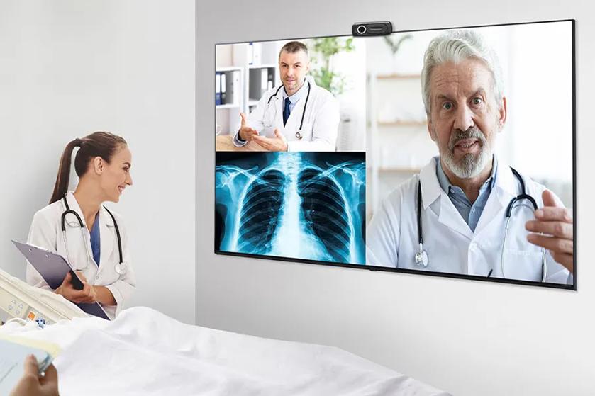 A doctor consulting via video conference with two other doctors and an X-ray on a screen.