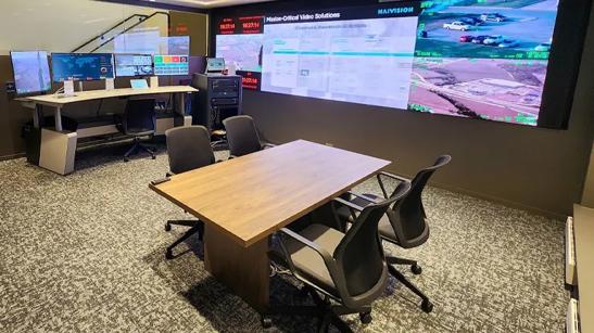 A meeting table beneath a large digital display in the LG DC Corporate Affairs Office. The display features sample surveillance and data readouts. A desk with IT monitors is in the background.