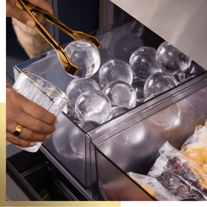 LG SIGNATURE refrigerator Big Craft Ice spheres in freezer drawer with scoop filling glass, close-up view.