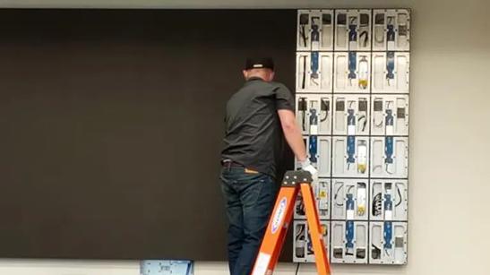 Worker stands on a ladder to install LG Direct View LED modules onto the panel cabinet. 