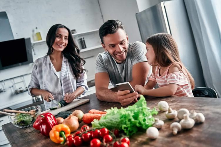 Family in kitchen preparing a meal with man and young girl looking at a mobile phone