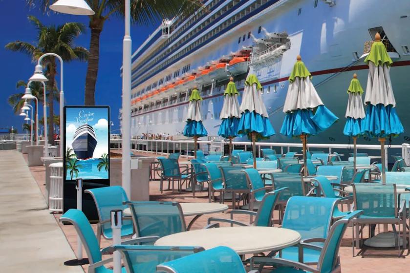 Sunny cruise port with LG outdoor display next to patio tables and chairs. A cruise ship is docked in the background.