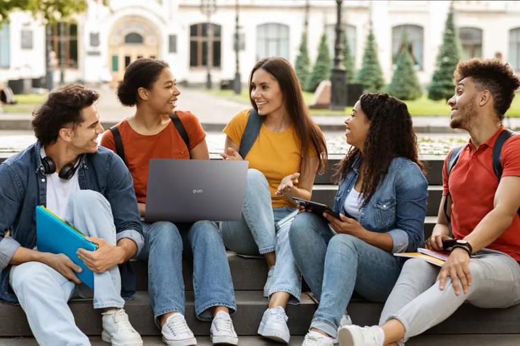 A group of five friends smile as they study outside on the quad. The woman in the middle has an LG gram laptop. 