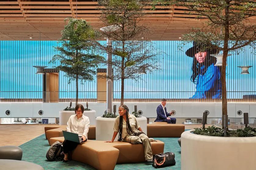 Airport patrons relax in the terminal's elegant lounge. Large scale Direct View LED covers the back wall, showing an image of a traveler and airplanes ,creating an elegant backdrop.