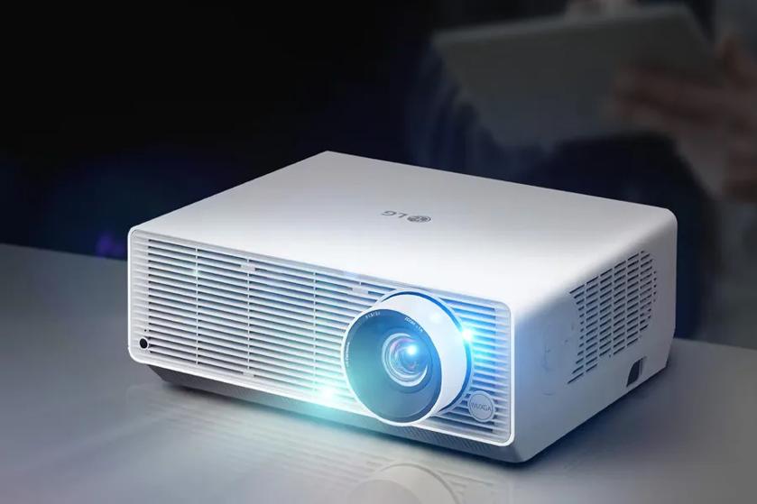 White projector with a bright blue lens on a reflective surface.