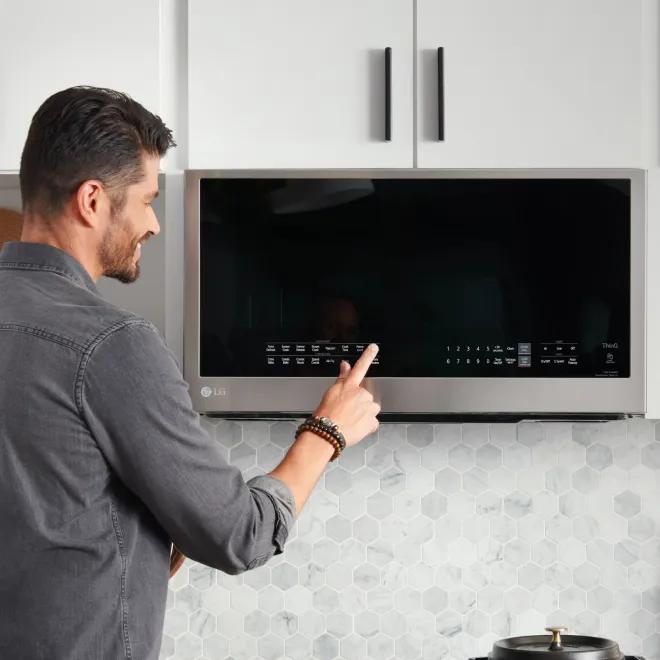 Man standing in front of an LG over-the-range microwave, pressing one of the. controls.