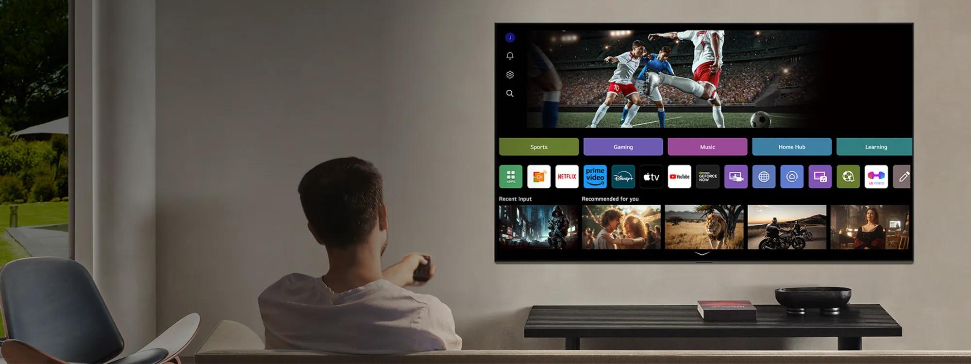 A man sits on a couch in a modern living room watching a large wall-mounted LG smart TV displaying an AI-enhanced home screen with various apps and streaming services.