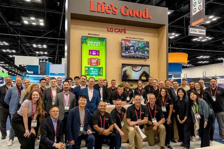 A group shot of all the LG employees attending the HITEC 2025 show, posing at the LG booth. The wall behind them has a large Life's Good slogan at the top, and is filled with LG displays. Beyond it, the rest of the event space is visible. Everyone is smiling at the camera.