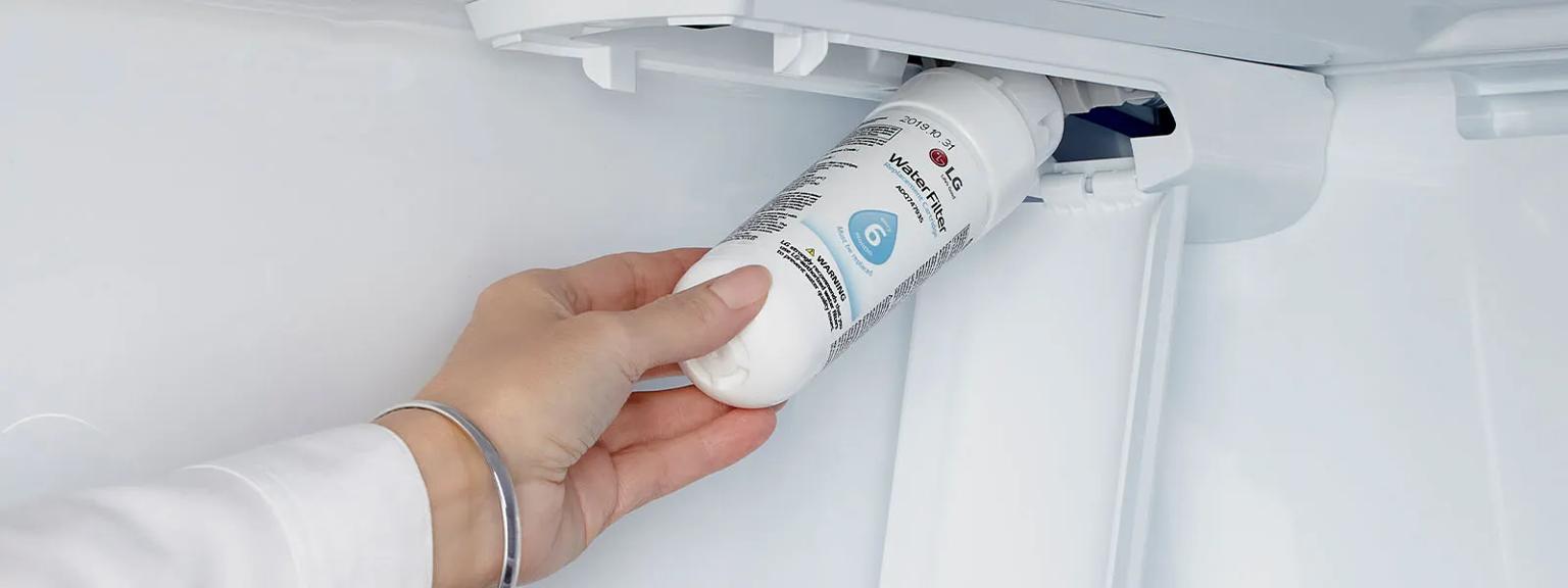 Hand reaching into a refrigerator water filter compartment holding water filter.