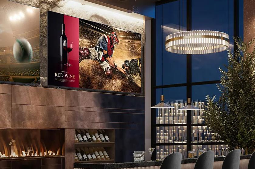 A bar area with screens displaying a baseball scene and red wine ad, under atmospheric lighting in a modern interior.
