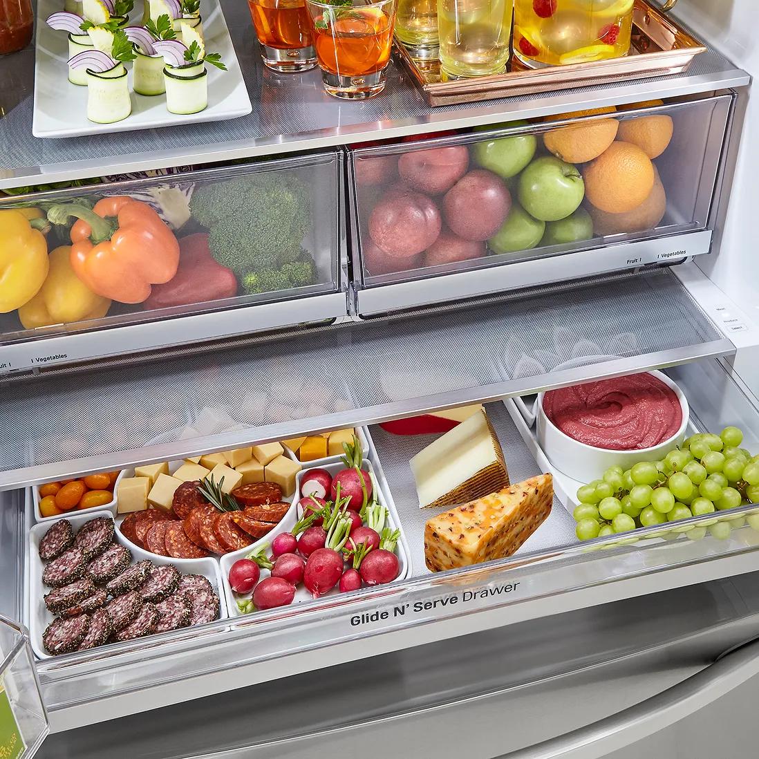 Inside LG 4-door French door refrigerator showing crispers filled with produce and a Glide N' Serve drawer stocked with meats, cheese, fruit, and snacks.