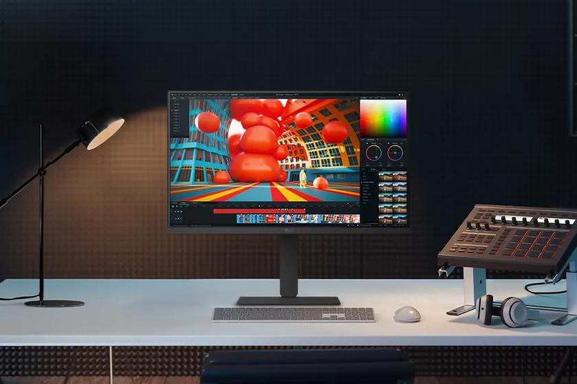 Front view of LG monitor on a desk, displaying a colorful 3D editing interface, with a lamp, keyboard, audio mixer, and headphones nearby.